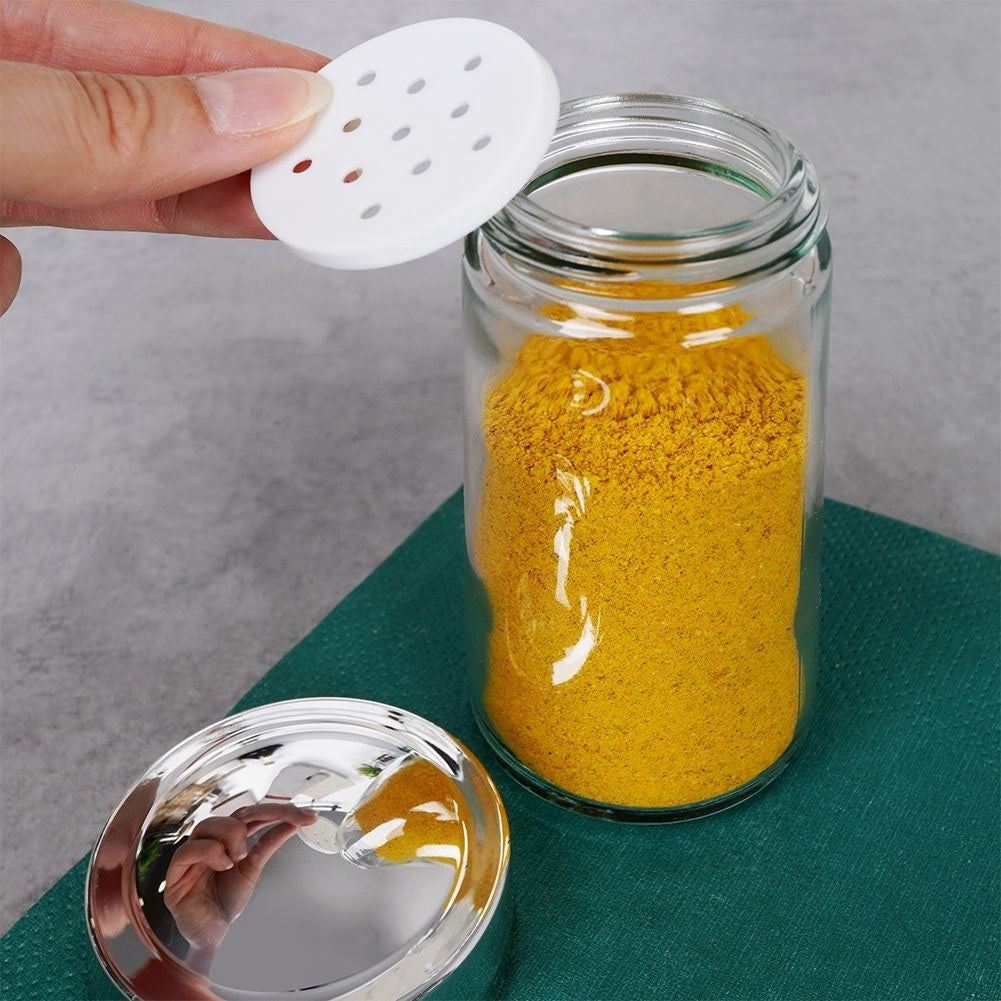 Un frasco de vidrio con polvo de especia amarillo. Se está colocando una tapa blanca perforada.