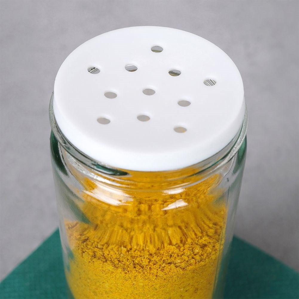 Un frasco de especias de vidrio lleno de polvo amarillo tiene una tapa blanca perforada.