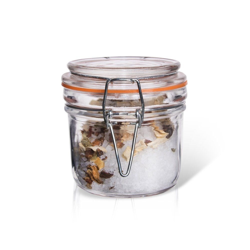 Tarro de cristal con especias y sal, con tapa abatible metálica y sello naranja.