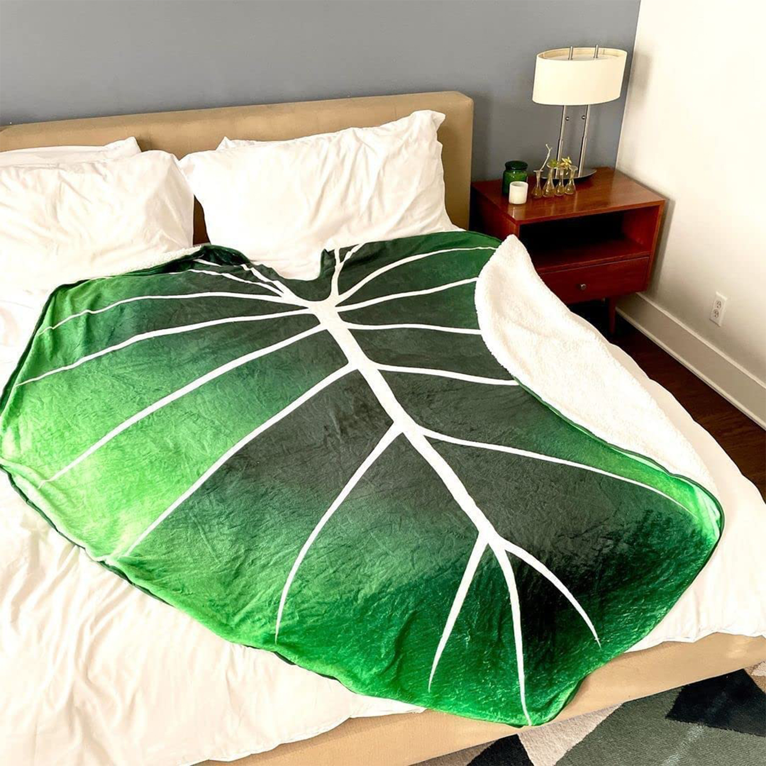 Coperta verde con stampa a foglia su letto con cuscini bianchi.