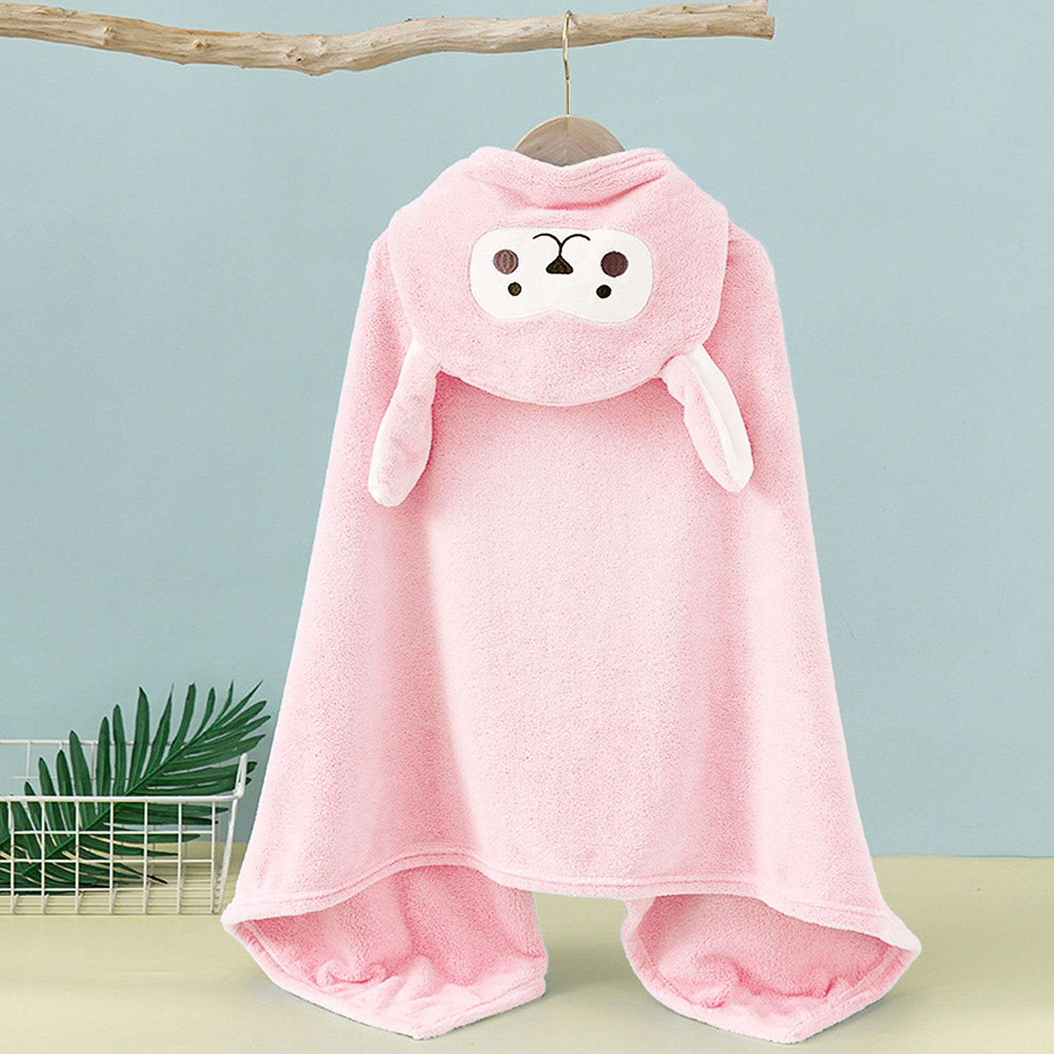Ein flauschiges, hellrosa Kapuzenhandtuch mit Schafgesicht hängt an einem Ast.