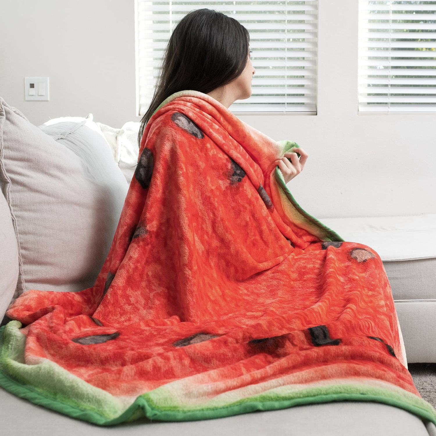 Una donna seduta su un divano, avvolta in una coperta a fantasia anguria.