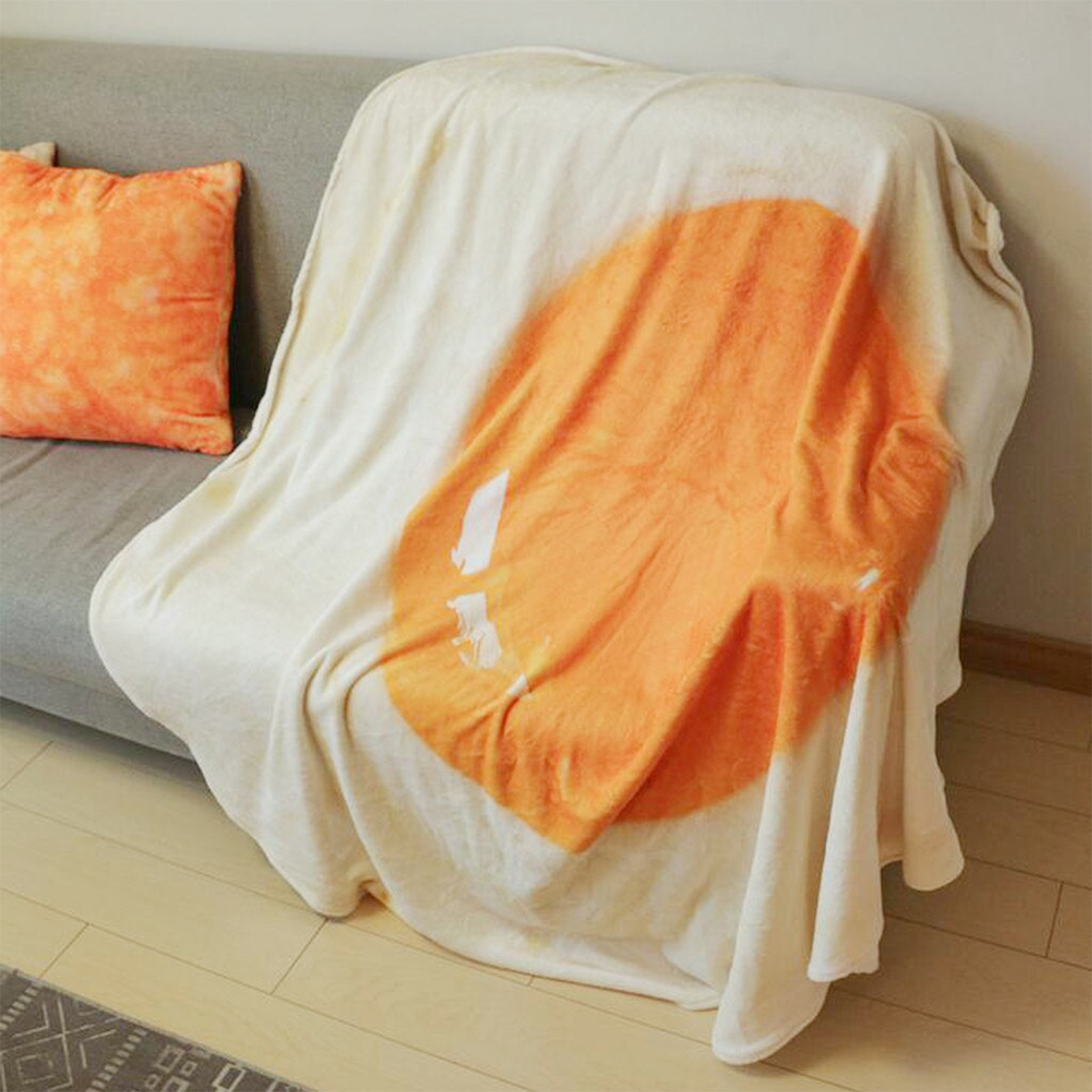 Una coperta con stampa di uovo fritto è su un divano accanto a un cuscino.