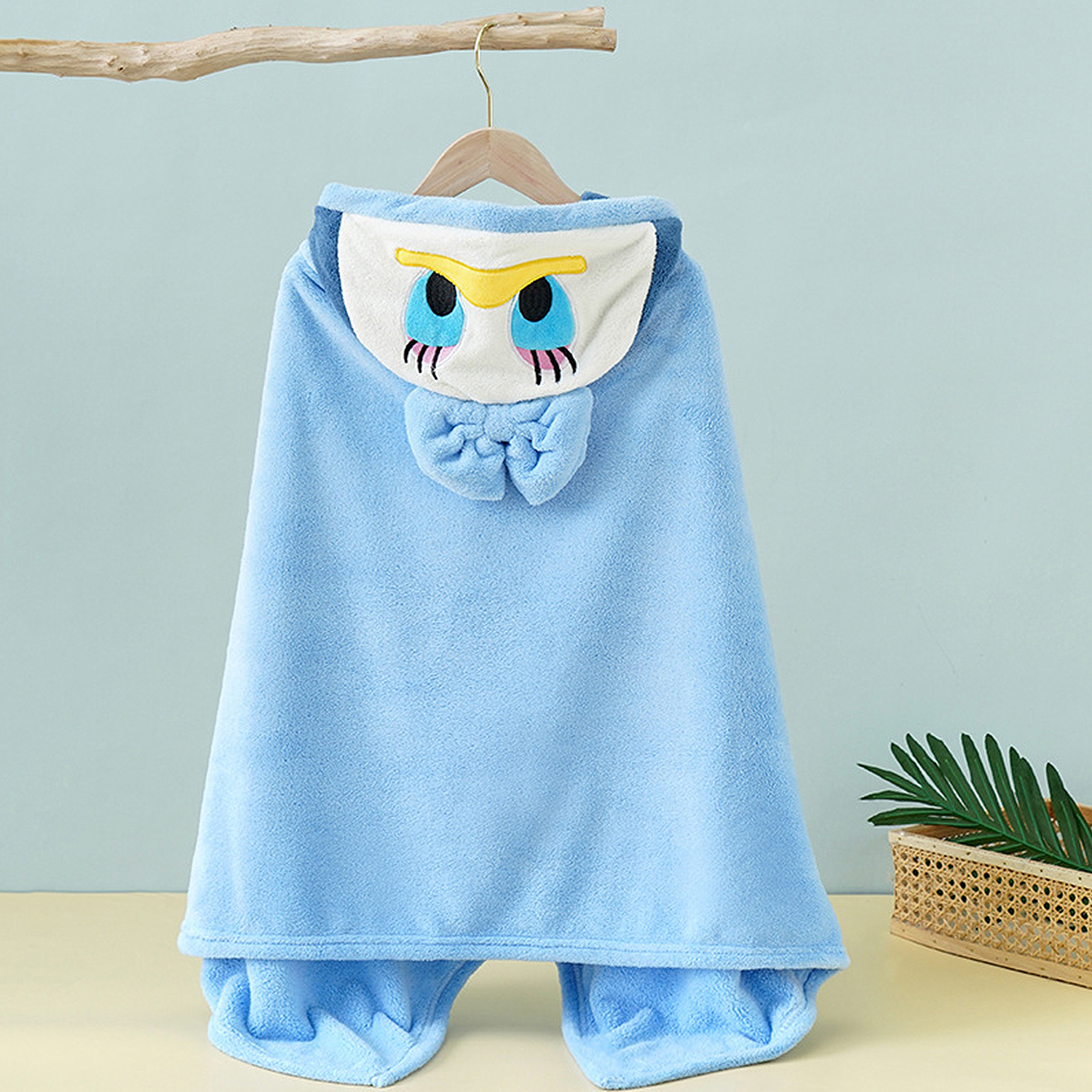 Ein hellblauer Kapuzenpullover mit einem Eulenmotiv, aufgehängt an einem Ast.