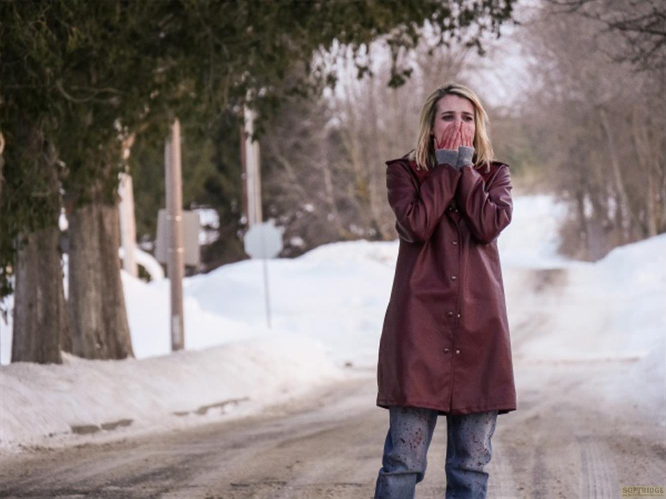 Une femme blonde se couvre la bouche de froid sur une route enneigée.