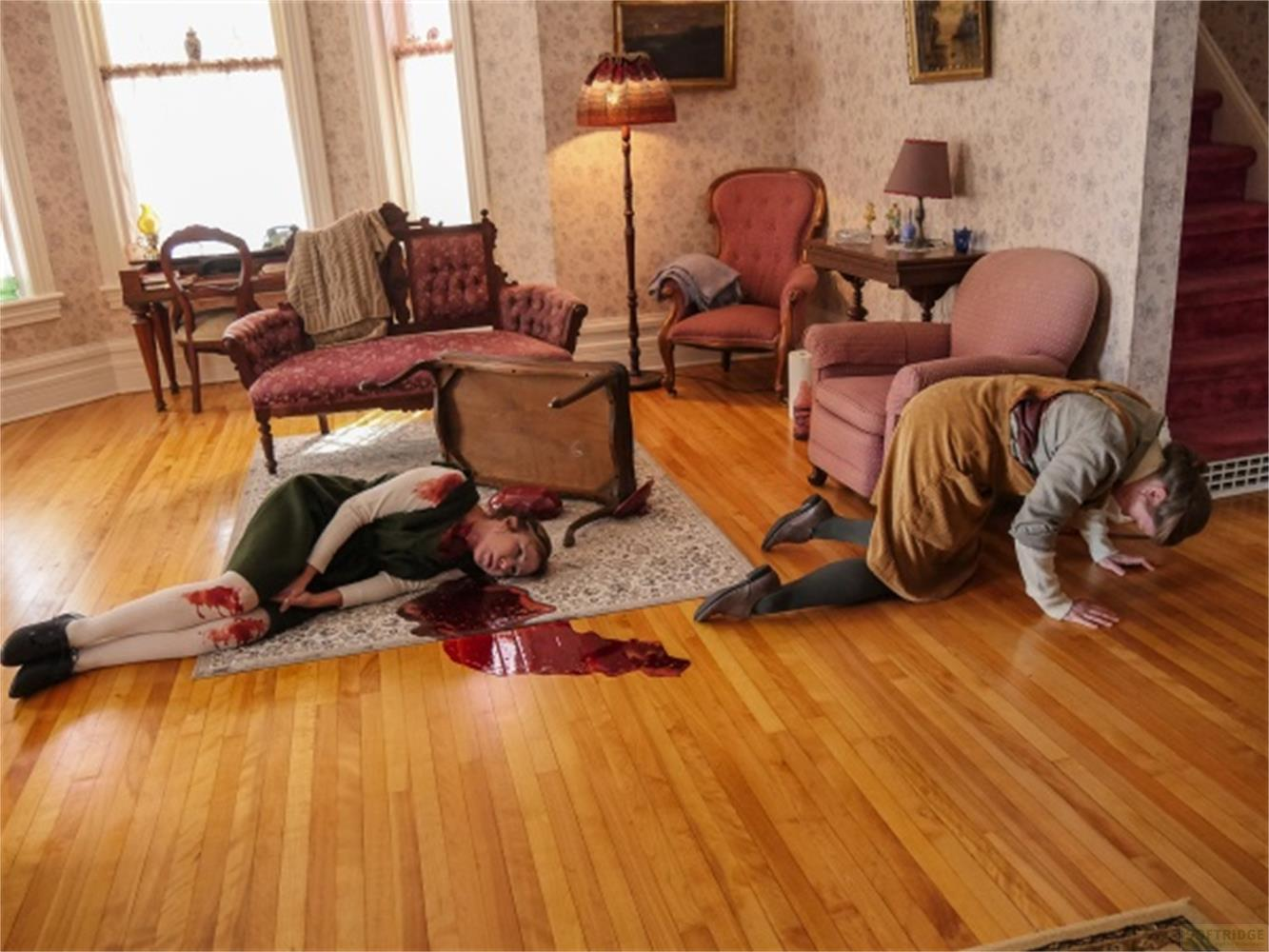 Deux femmes gisent au sol, l'une blessée. Une table renversée.