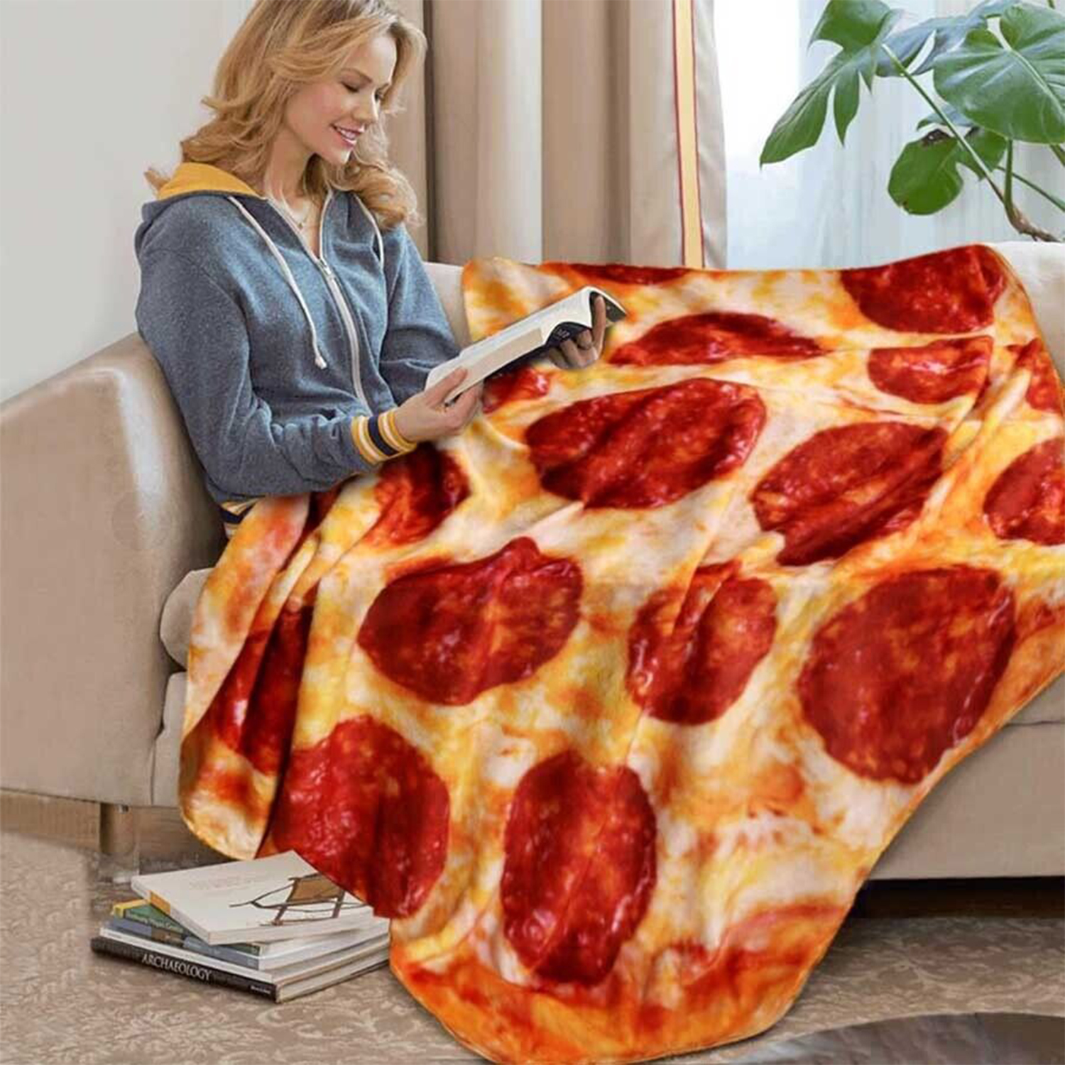 Eine Frau sitzt auf einer Couch und liest ein Buch, zugedeckt mit einer Pizza-Decke.