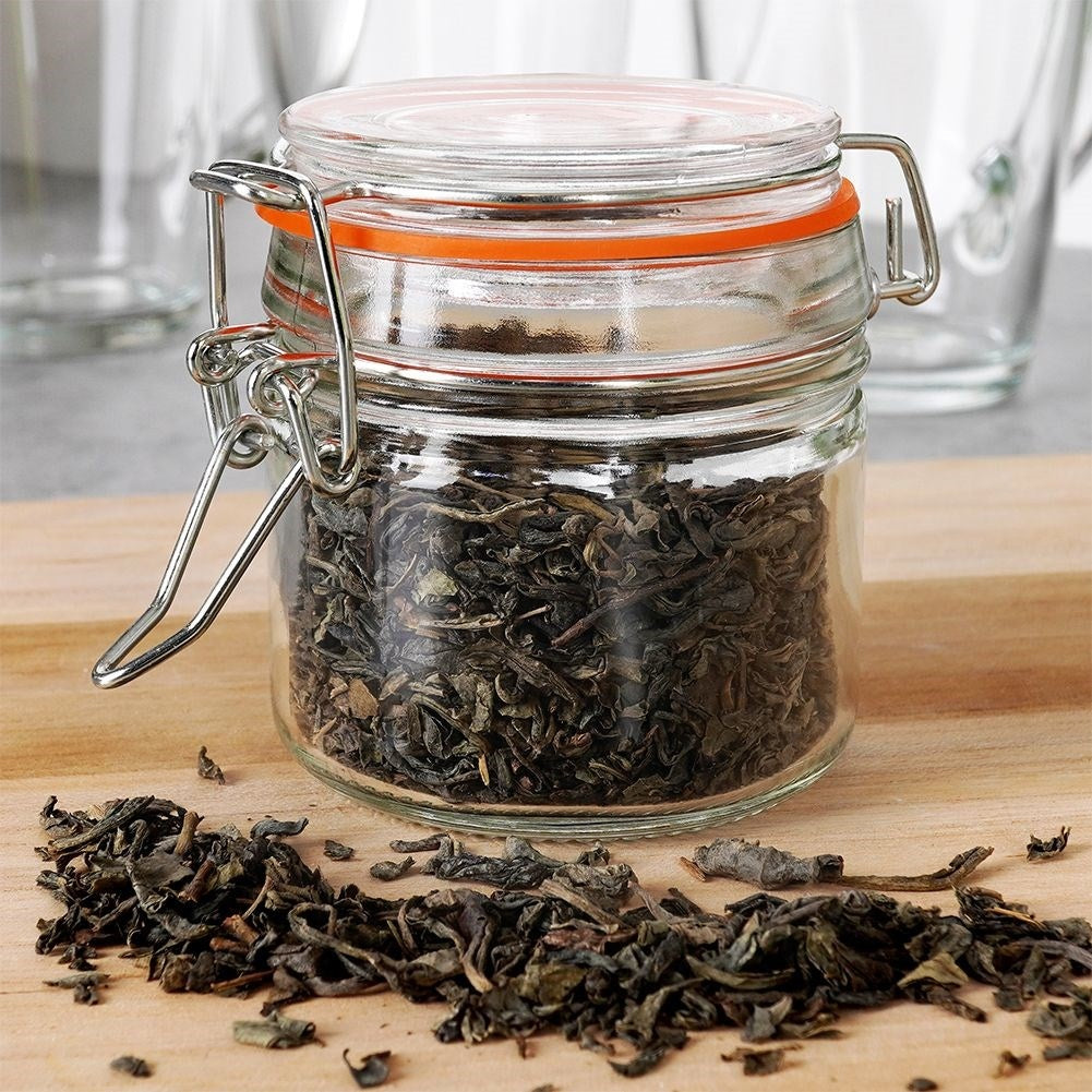 Un frasco de vidrio con hojas de té secas y clips metálicos, con hojas esparcidas.