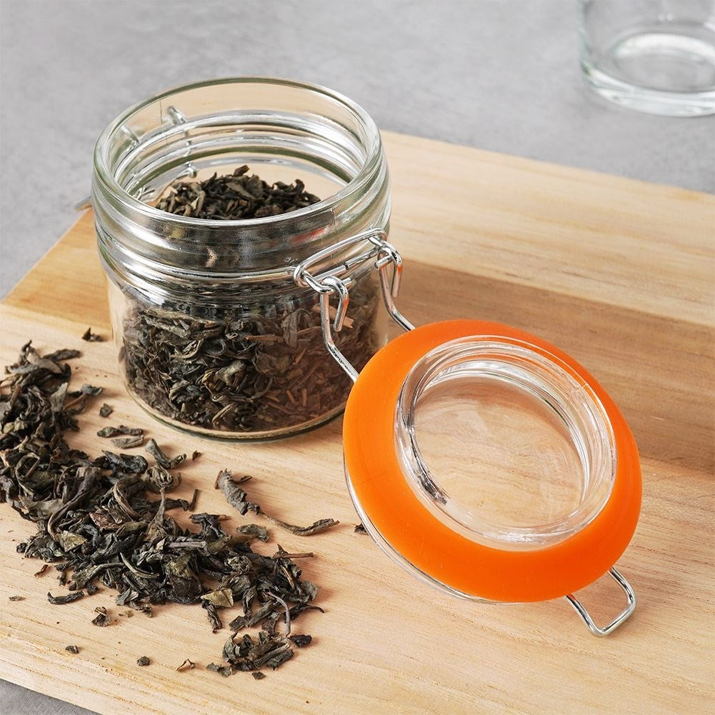 Un frasco de vidrio con té suelto y tapa naranja abierta sobre tabla de madera.