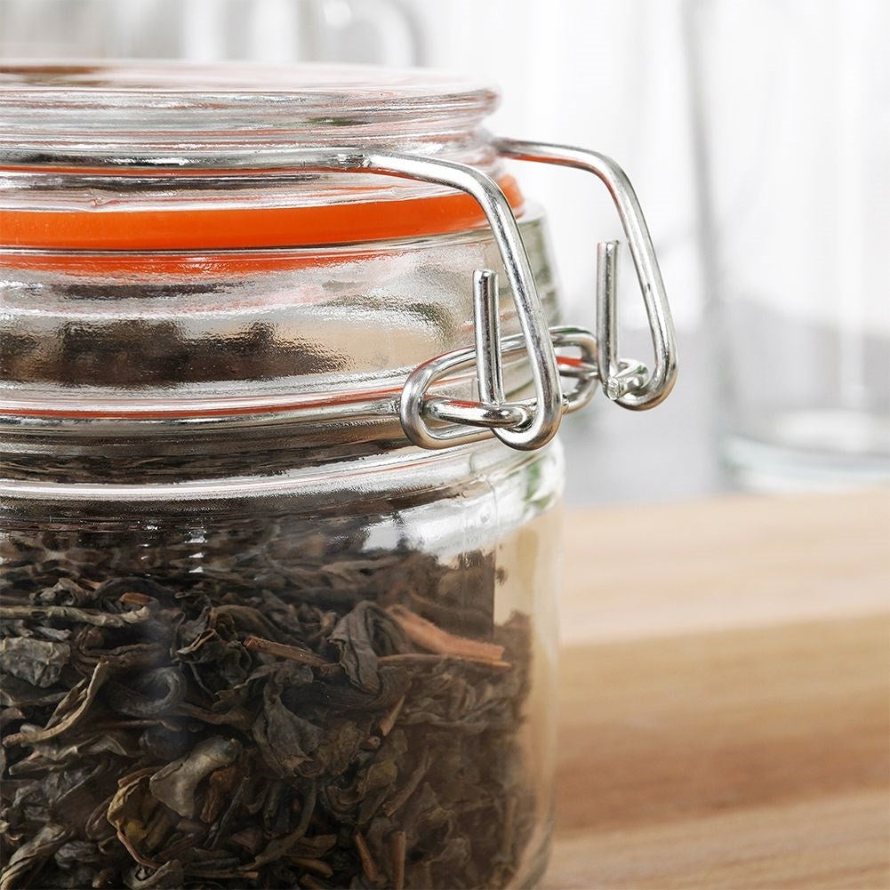 Un frasco de vidrio con hojas de té secas, sello naranja y cierre de alambre.