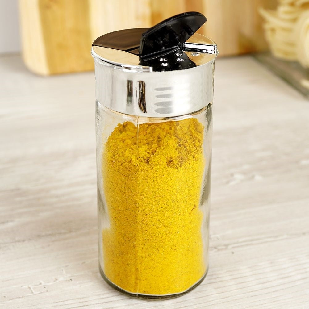 Un salero de vidrio lleno de polvo amarillo y tapa negra.