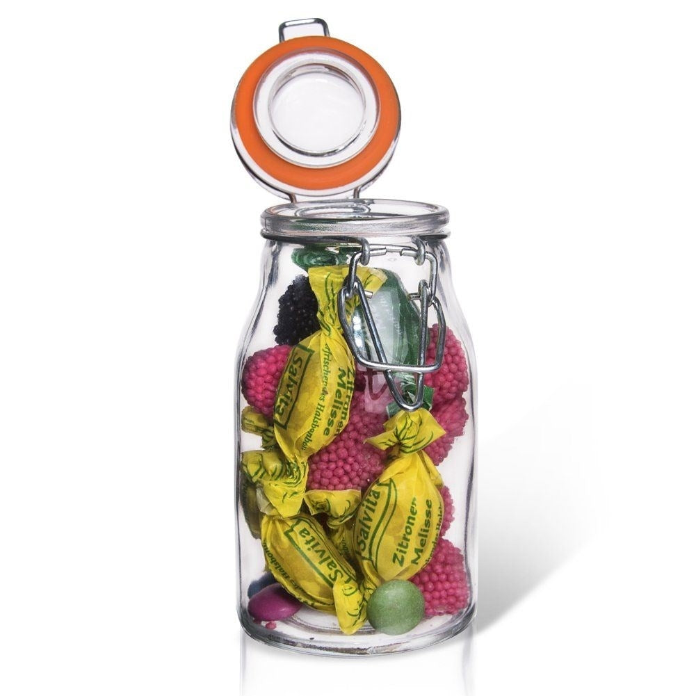 Tarro de cristal lleno de caramelos amarillos, rosas y verdes, con moras y frambuesas.