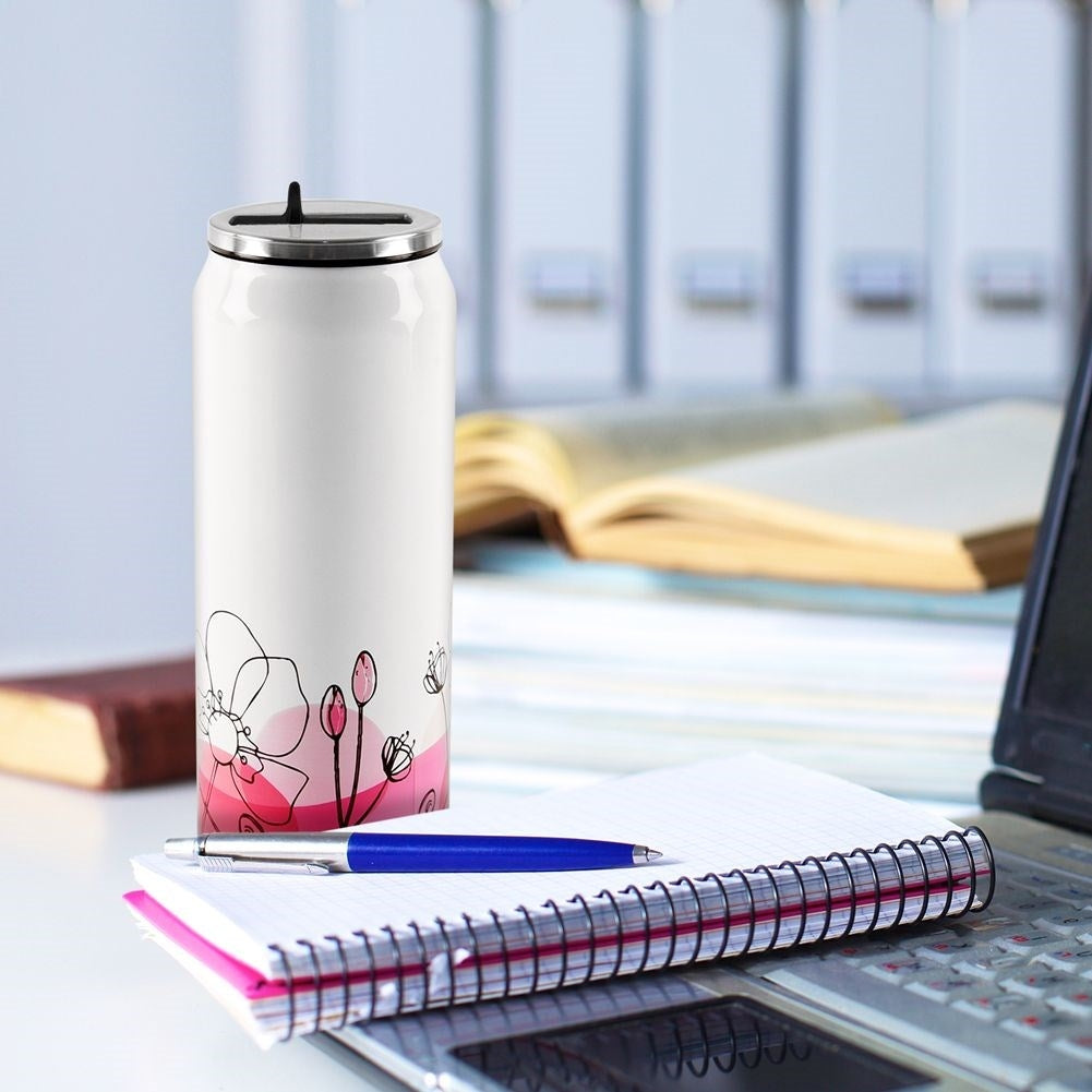 Una taza blanca con estampado floral sobre un cuaderno junto a un portátil.