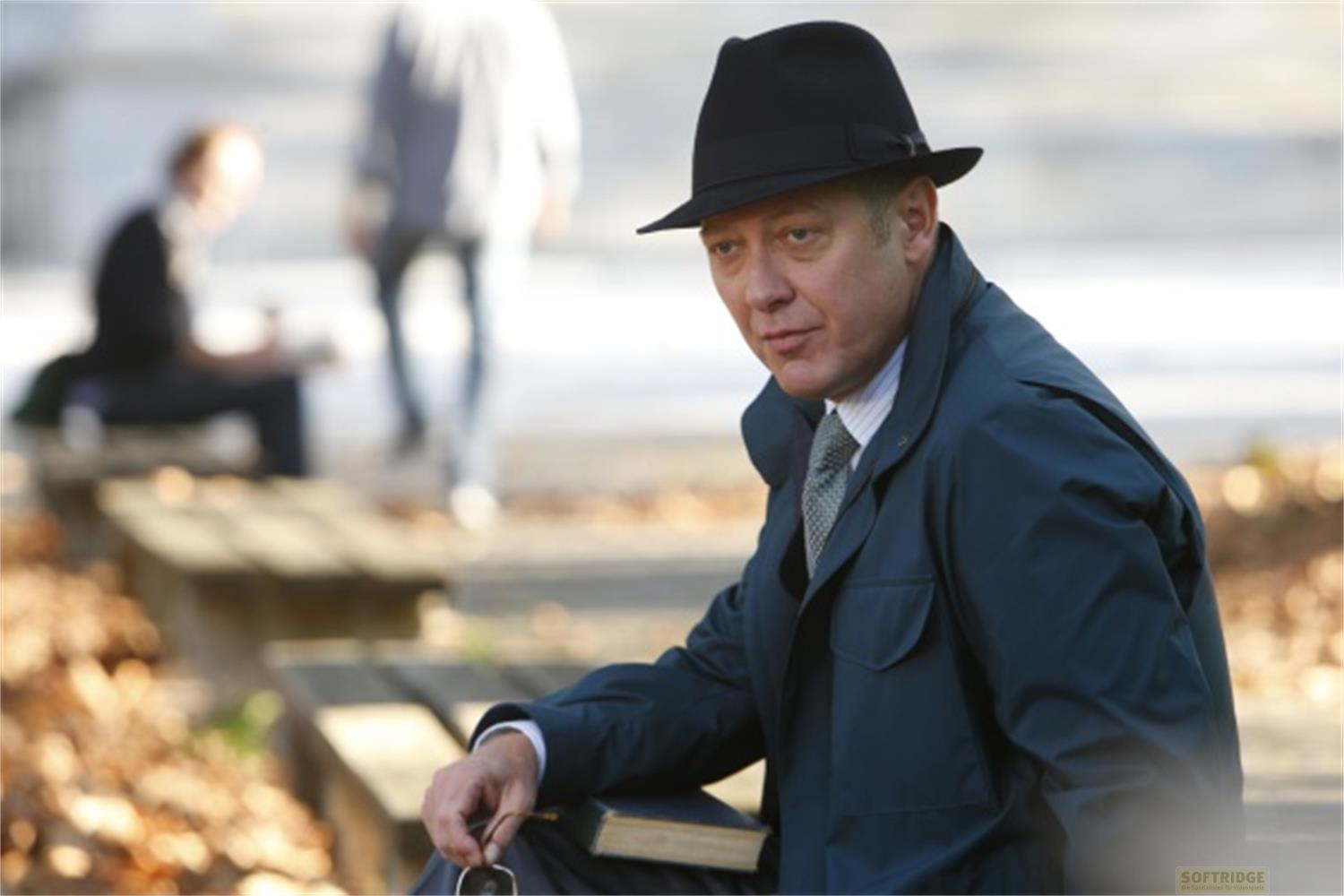 Un uomo con cappello e cappotto siede all'aperto su una panchina con un libro.
