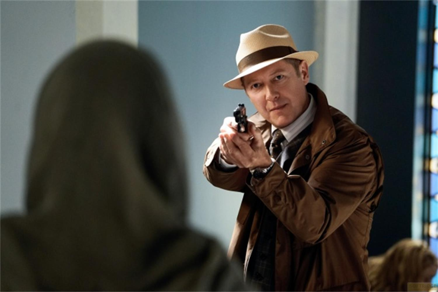 Uomo con cappello punta pistola verso persona sfocata in primo piano.