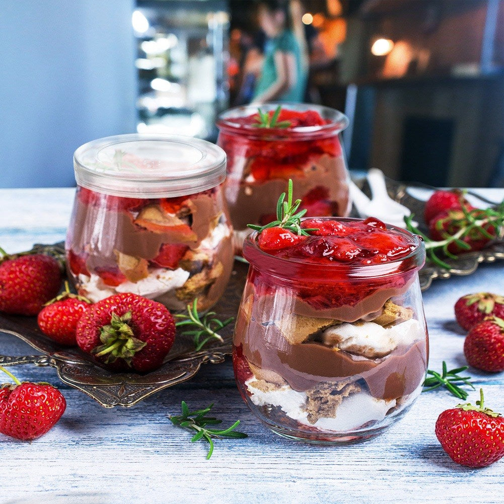 Tres tarros con postre de chocolate y fresas, adornados con romero.