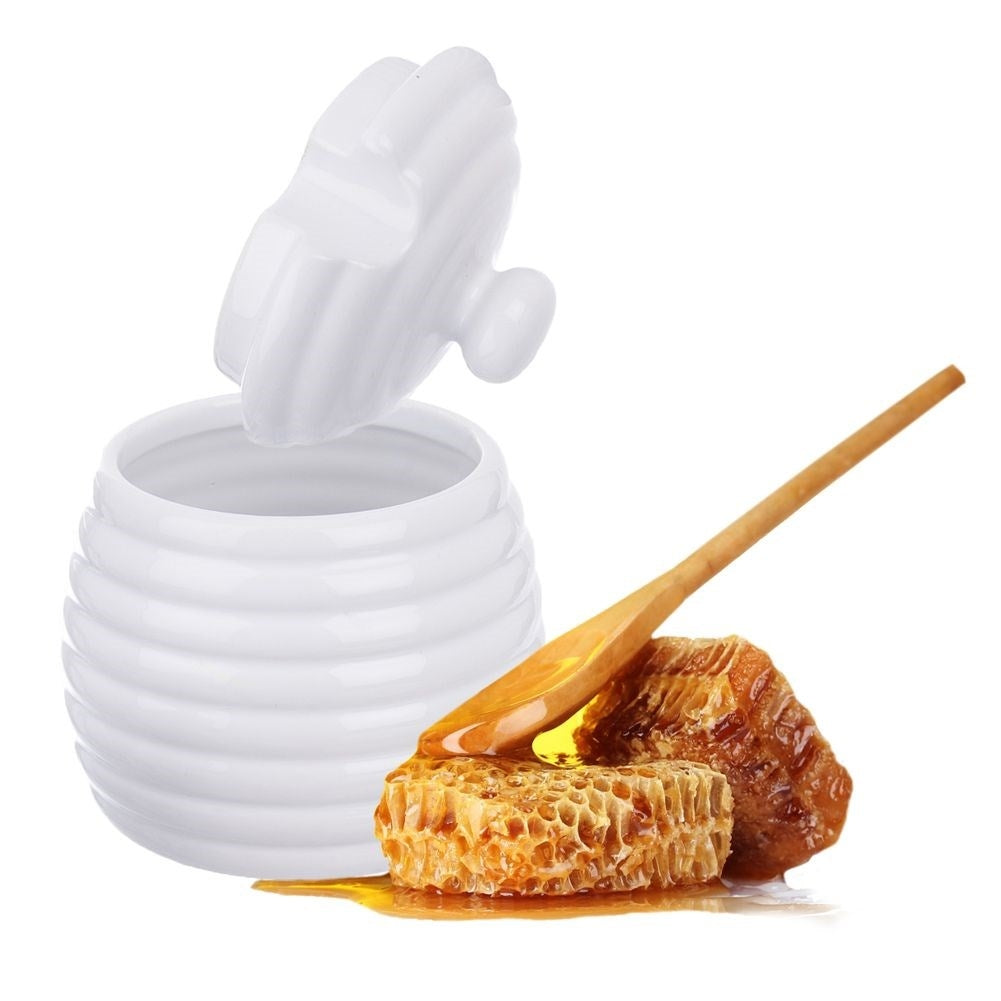 Una mielera blanca con panal y un gotero de madera.