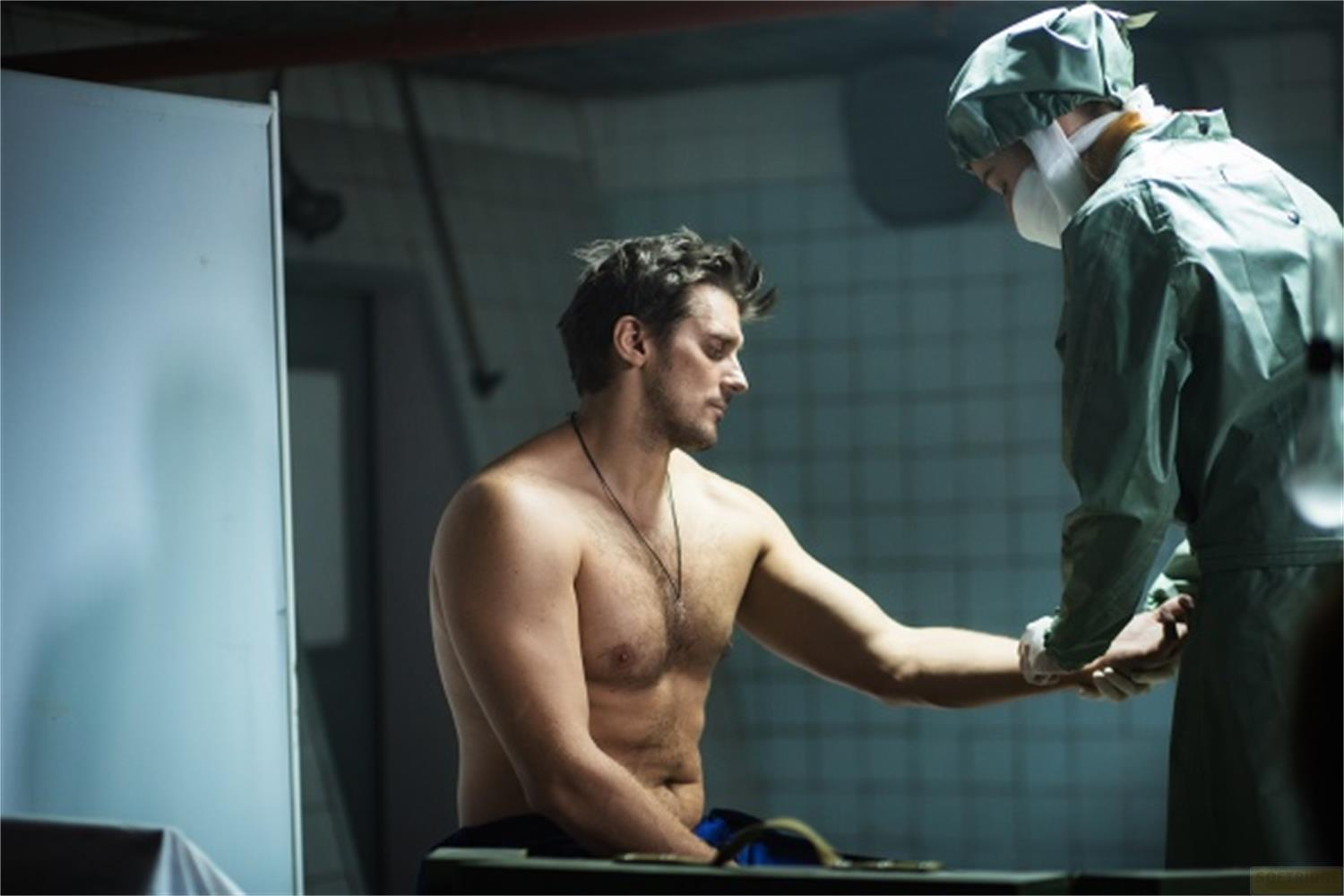 Un uomo in abiti chirurgici esamina il braccio di un uomo a torso nudo.