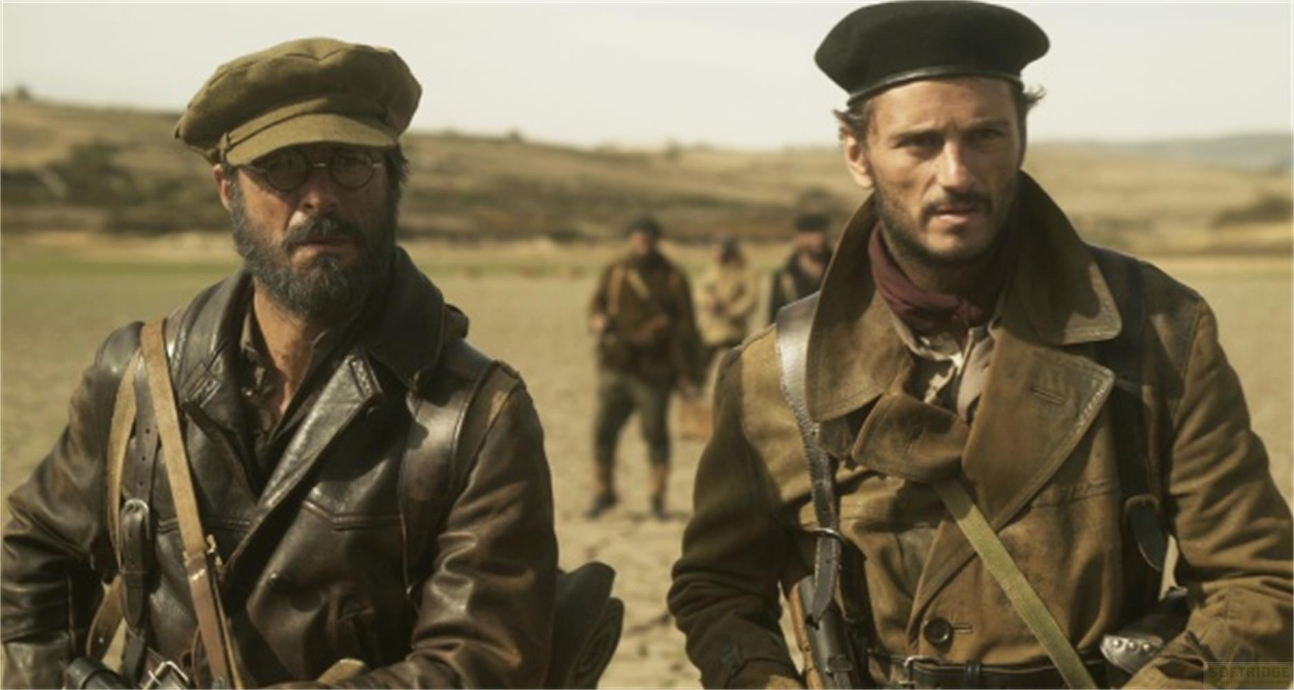 Due uomini in abiti militari camminano in un paesaggio arido. Uno indossa una giacca di pelle, l'altro un cappotto.
