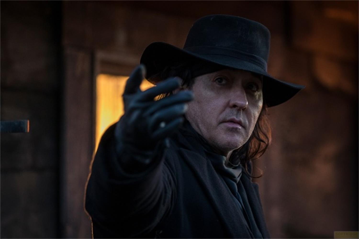 Un uomo con cappello nero e guanti allunga la mano.