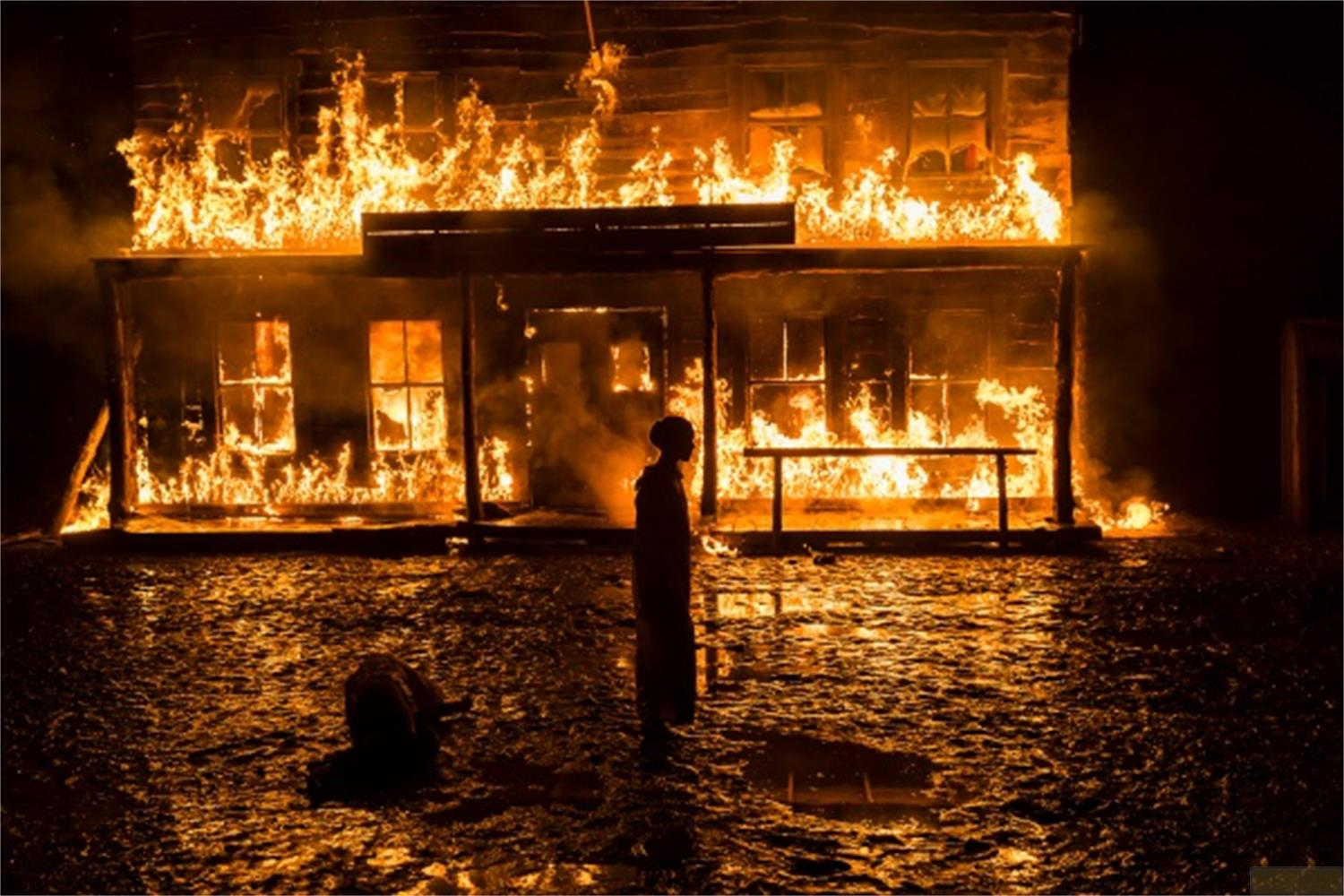 Un edificio brucia di notte. Una persona è davanti nell'acqua.
