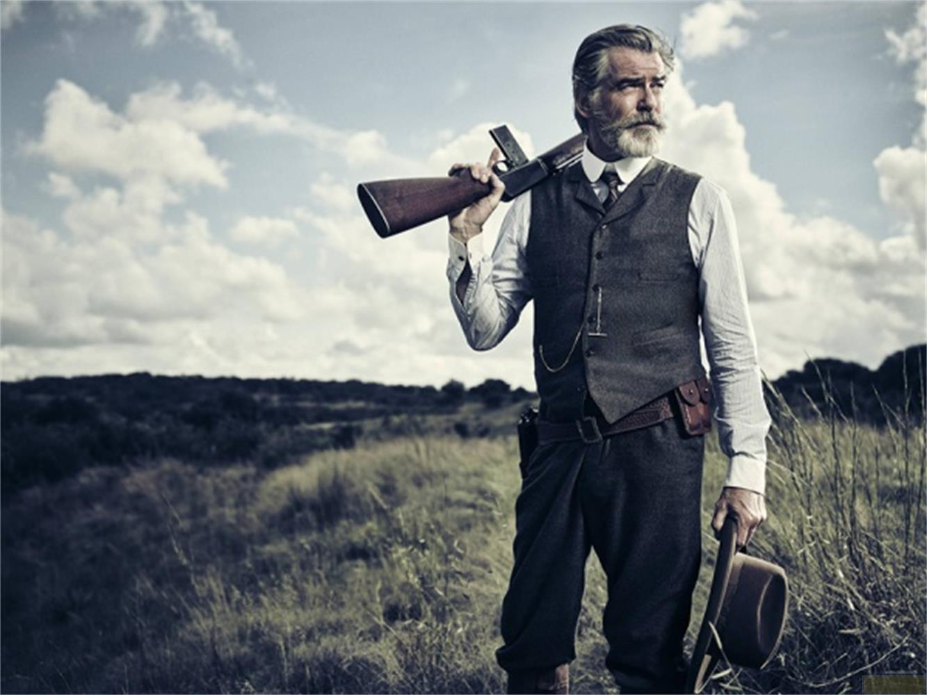 Un uomo con la barba grigia indossa gilet, camicia e pantaloni. Porta un fucile sulla spalla.