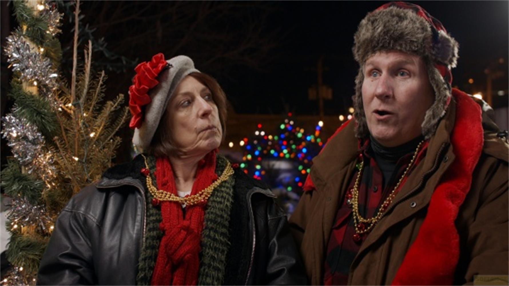 Uomo e donna in abiti invernali davanti a un albero di Natale e luci.