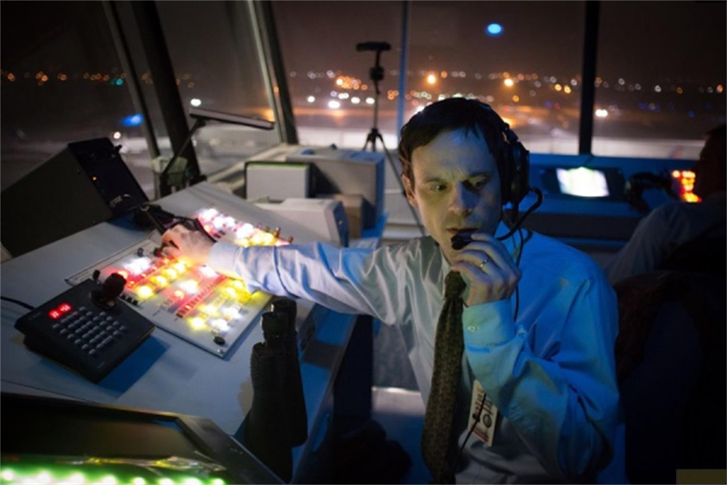 Uomo nella torre di controllo dell'aeroporto di notte, parla al microfono.