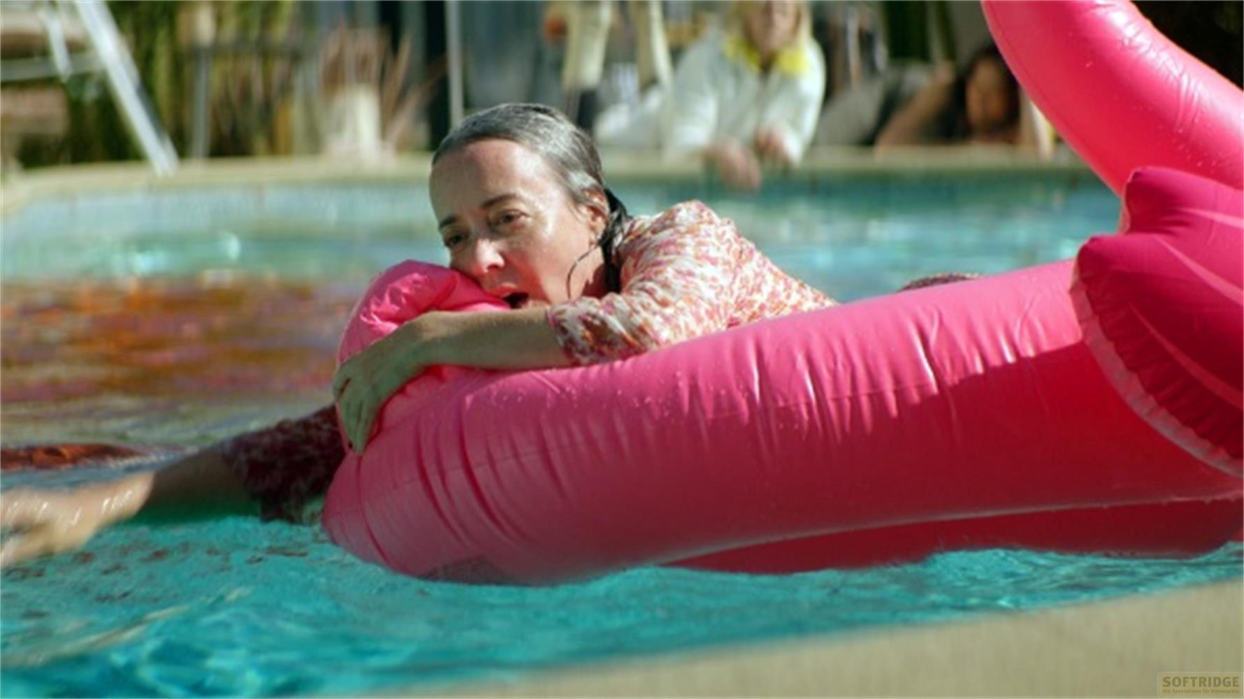 Una donna nuota in piscina su un gonfiabile a forma di fenicottero rosa.