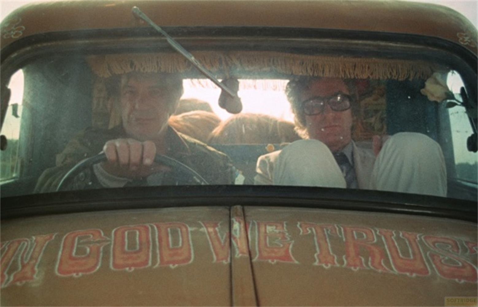 Due uomini in un'auto, con "IN GOD WE TRUST" scritto sul cofano.