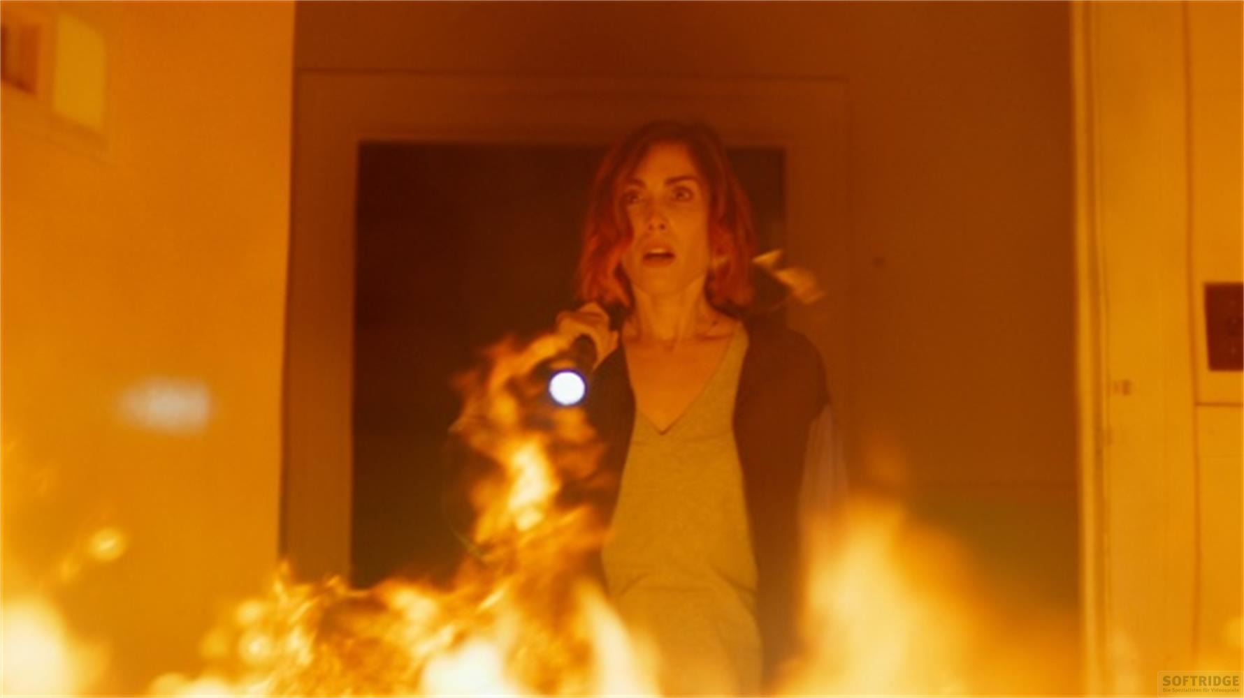 Una donna con una torcia si trova tra le fiamme davanti a una porta.