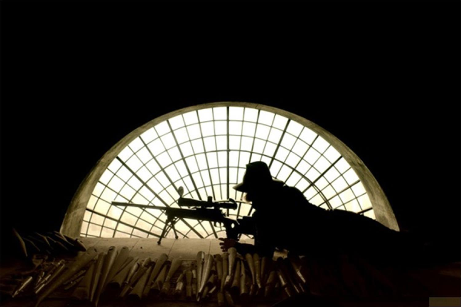 Silhouette di un tiratore con fucile davanti a una finestra ad arco con griglia.