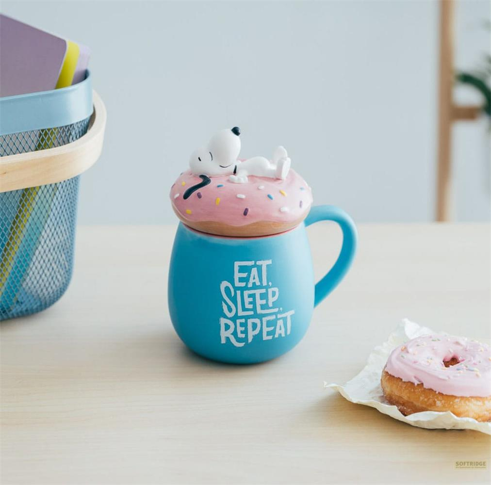 Blaue Tasse mit Snoopy auf einem Donutdeckel, daneben ein Donut.