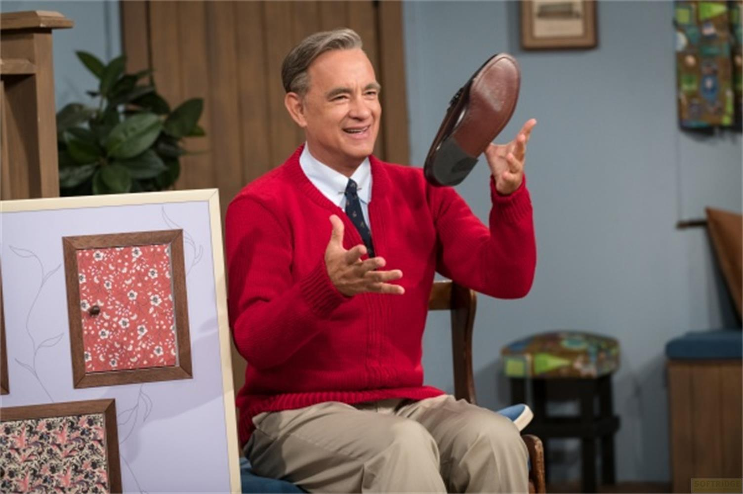 Tom Hanks tiene una scarpa marrone, indossa un maglione rosso e una cravatta.
