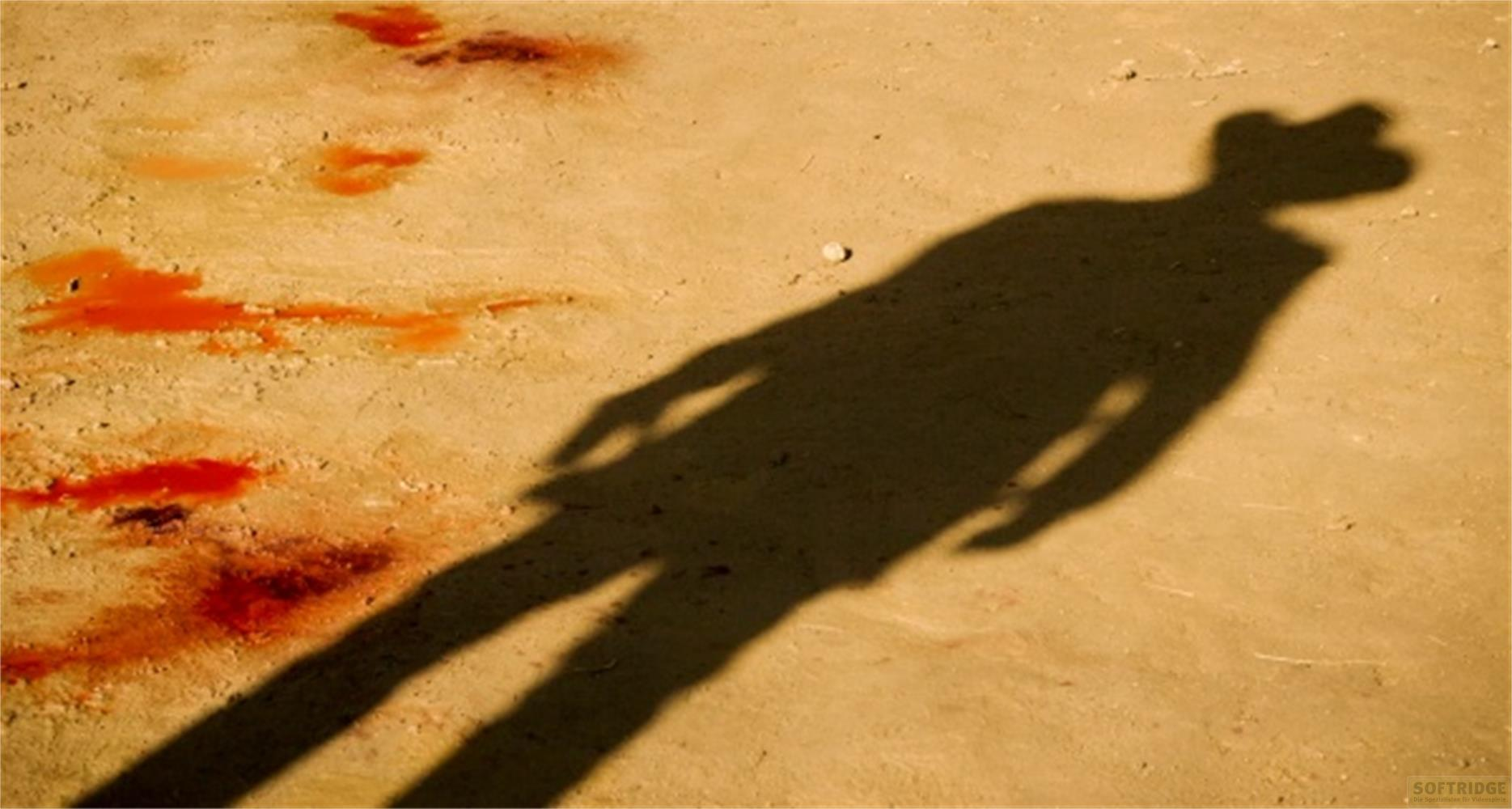 Ombre d'une personne avec un chapeau sur un sol sablonneux avec des taches rouges.