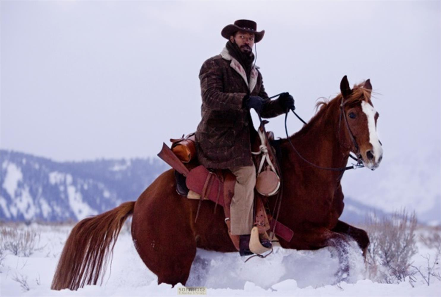 Un homme en tenue de cow-boy monte un cheval brun dans la neige profonde.