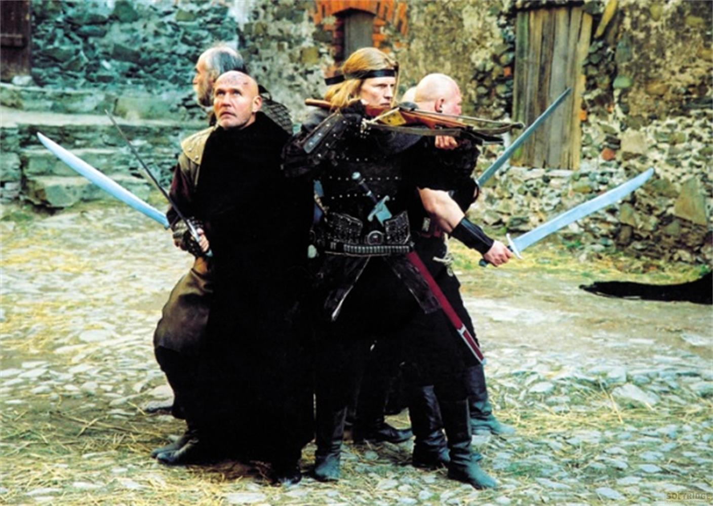 Quattro uomini in costumi storici con spade e balestra davanti a mura di pietra.