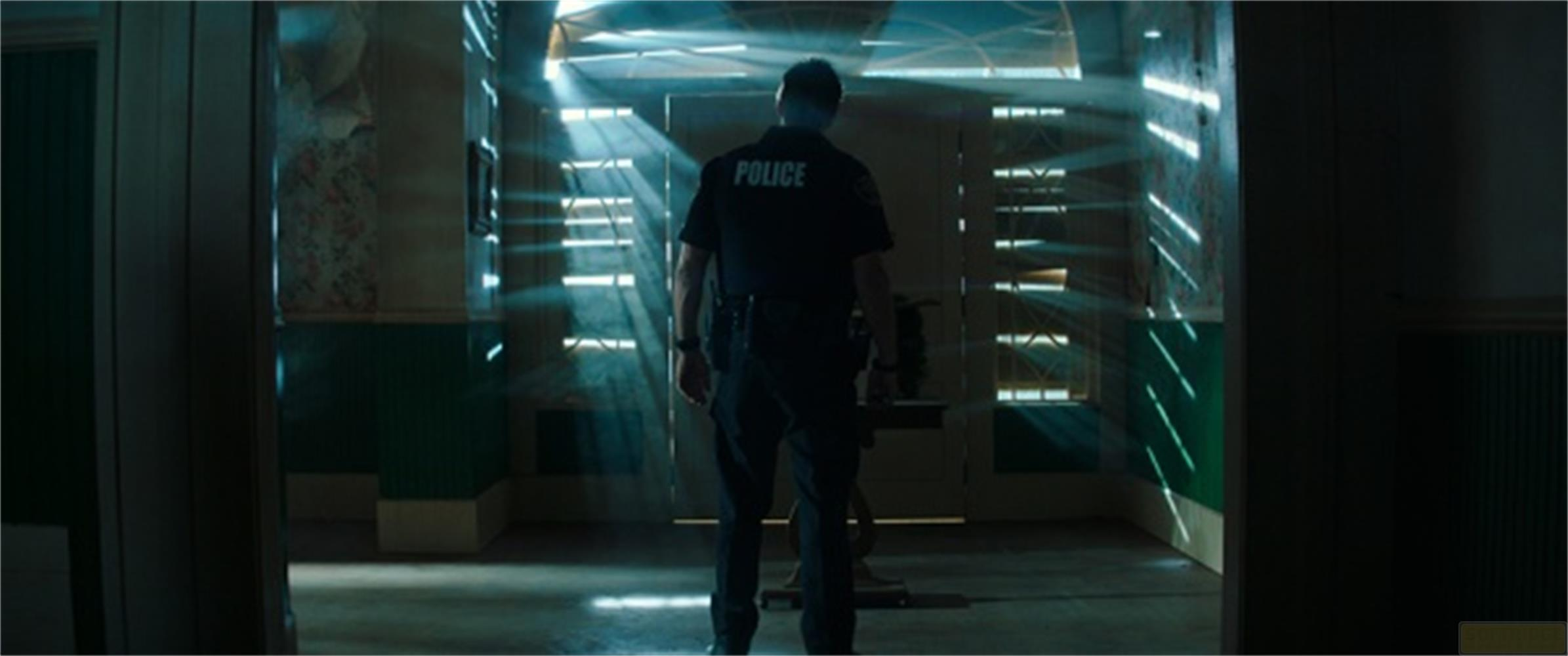 Un poliziotto in uniforme scura si trova in una stanza con luce a strisce.