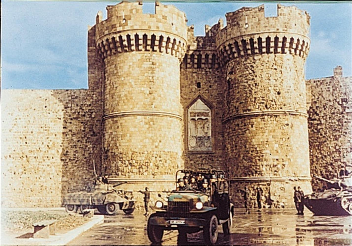 Véhicules militaires et soldats devant un ancien château de pierre à deux tours.