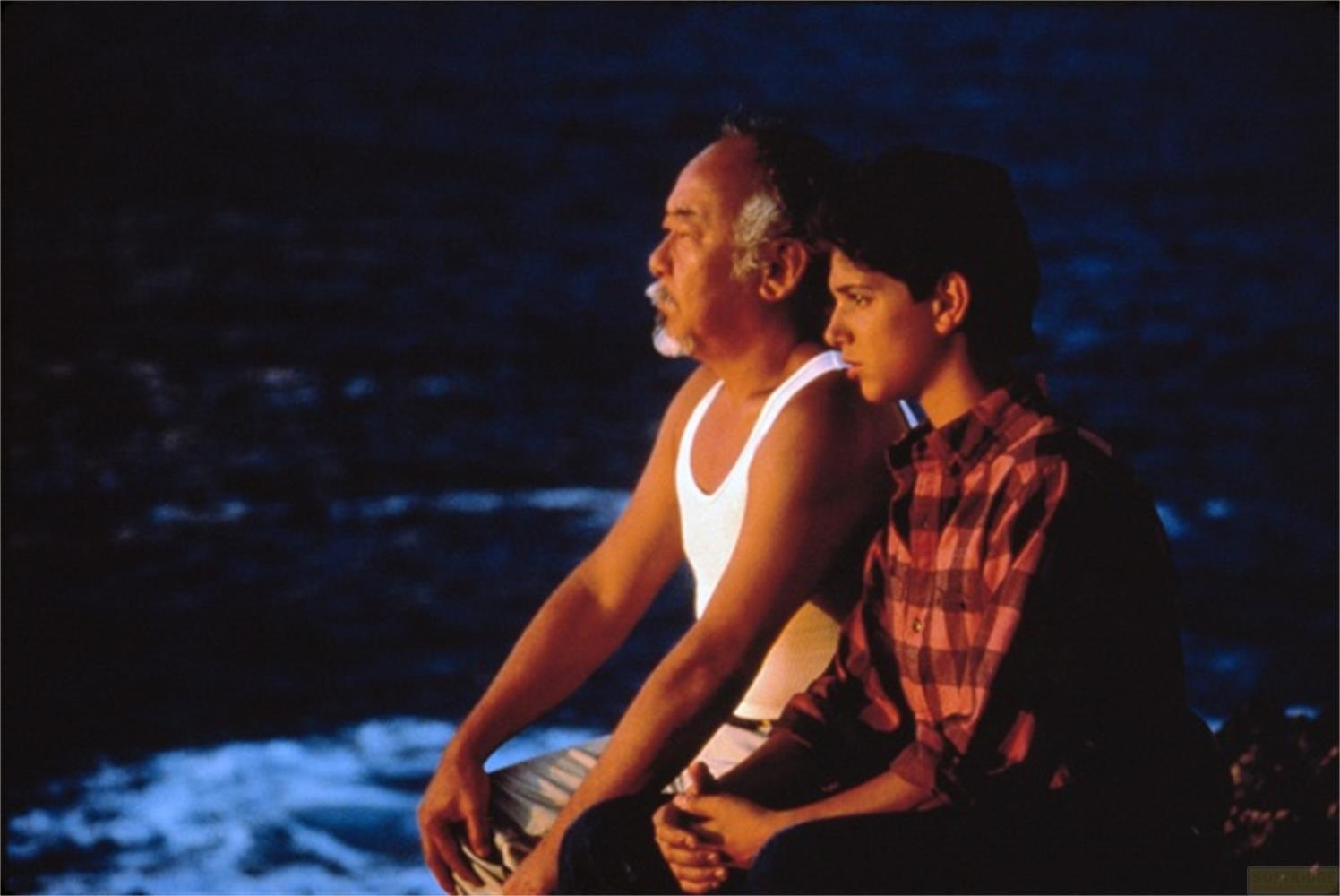 Un homme âgé et un adolescent assis côte à côte près de l'eau.