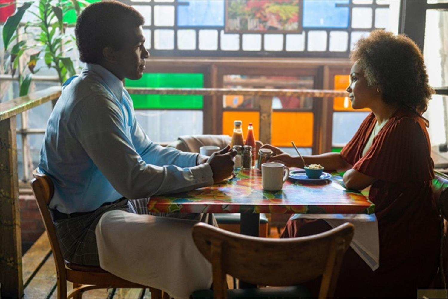 Un uomo e una donna siedono uno di fronte all'altro a un tavolo colorato in un caffè.