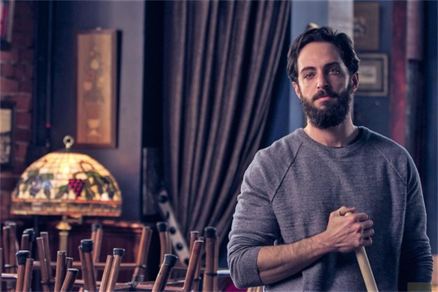 Uomo con barba in maglione grigio che tiene una stecca da biliardo in stanza.