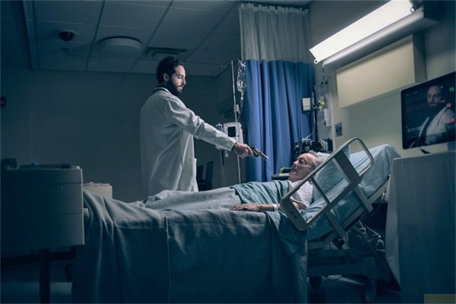 Un medico punta una pistola contro un paziente in un letto d'ospedale.