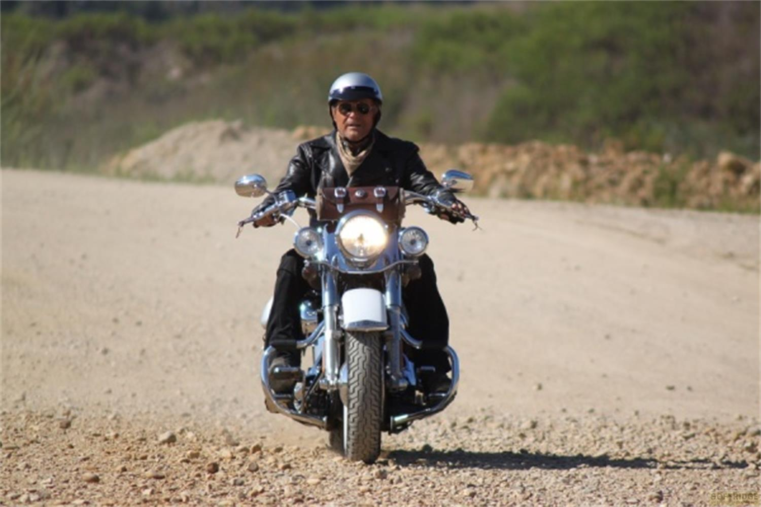 Un uomo guida una moto su una strada sterrata, indossa giacca di pelle e casco.
