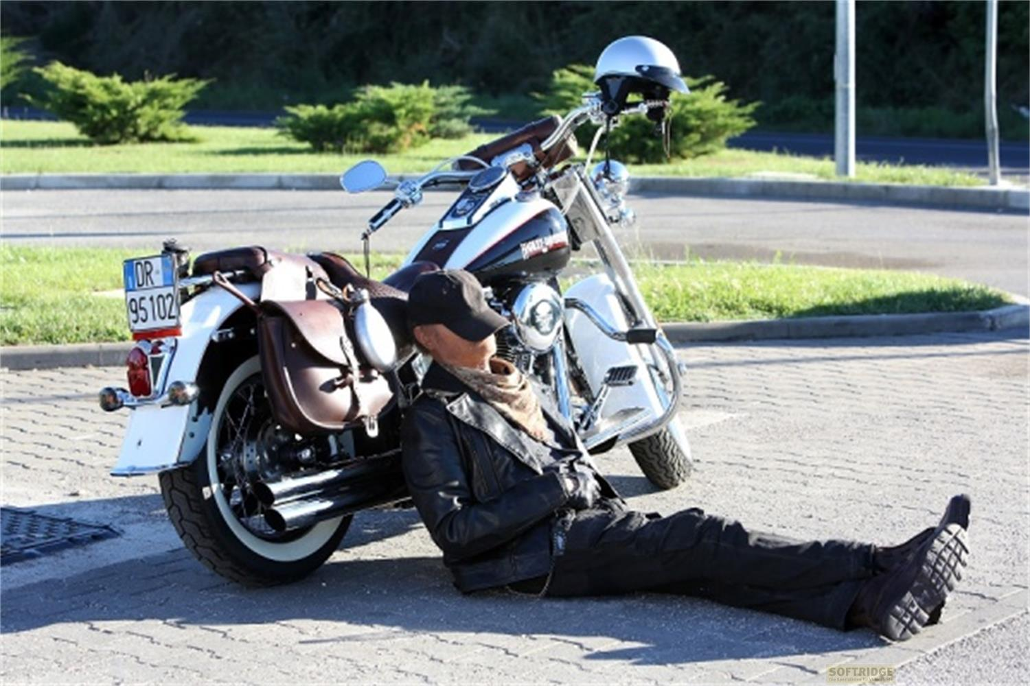 Un uomo in abiti di pelle si appoggia a una moto parcheggiata su un sentiero lastricato.