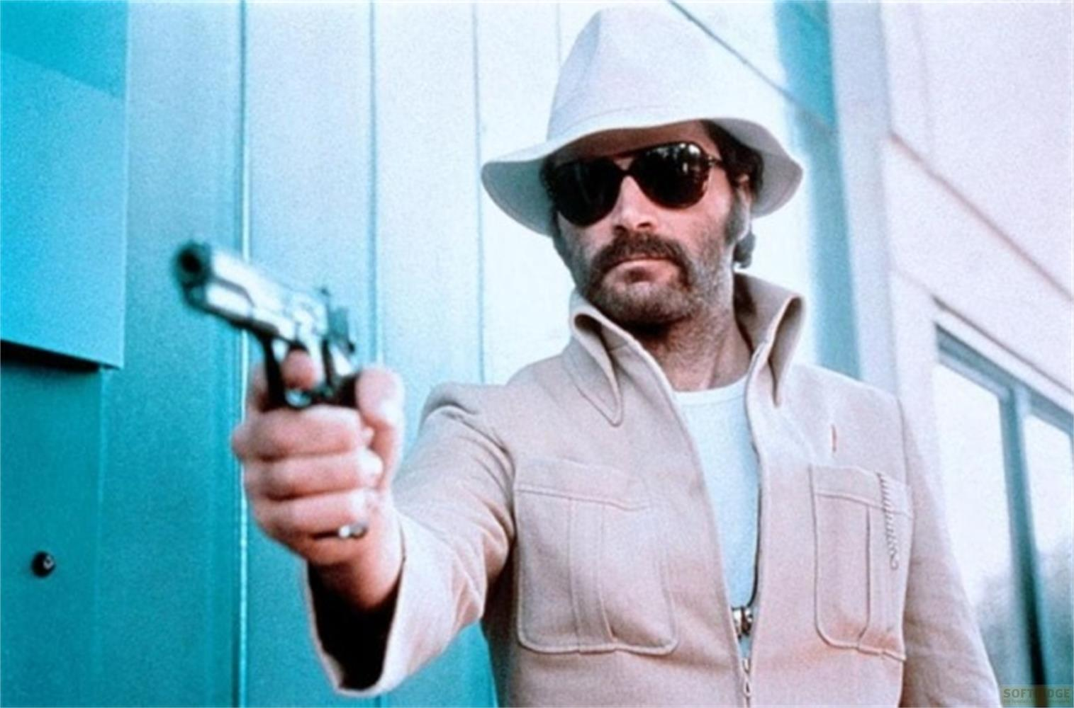 Uomo con cappello e occhiali da sole tiene una pistola all'aperto.
