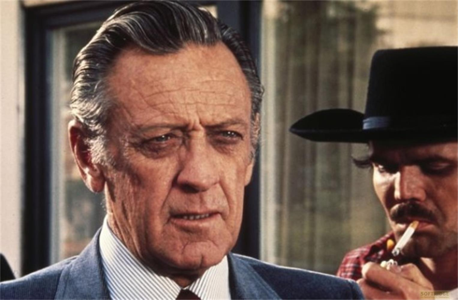 Due uomini conversano; uno indossa un cappello e fuma, l'altro un abito.