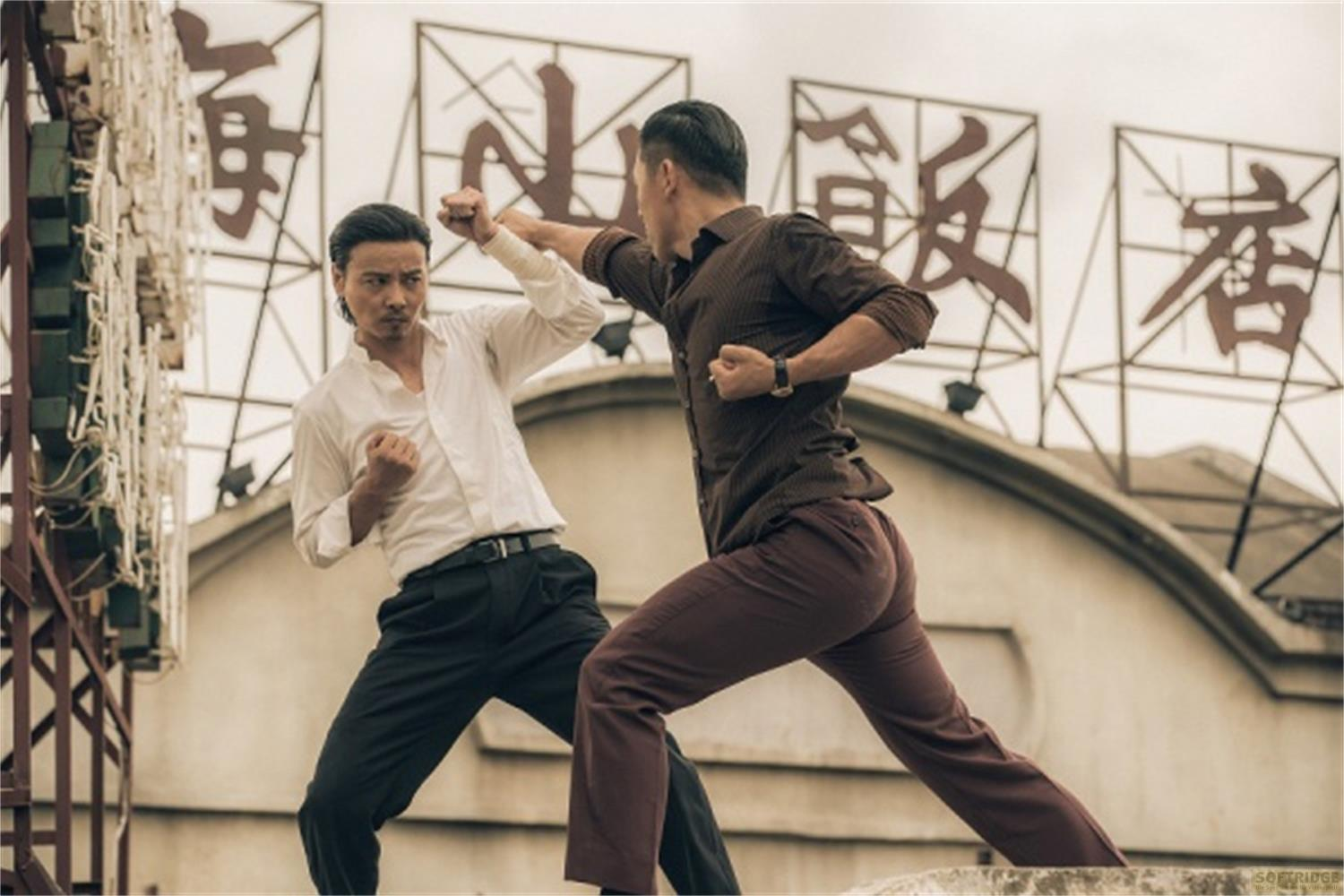 Due uomini in una scena di combattimento con caratteri cinesi sullo sfondo. Uno indossa bianco, l'altro marrone.