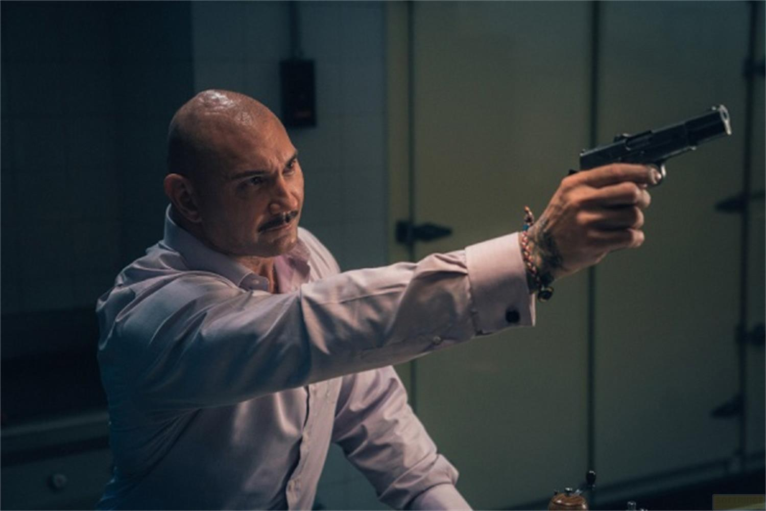 Un uomo calvo punta una pistola, indossa una camicia rosa chiaro.