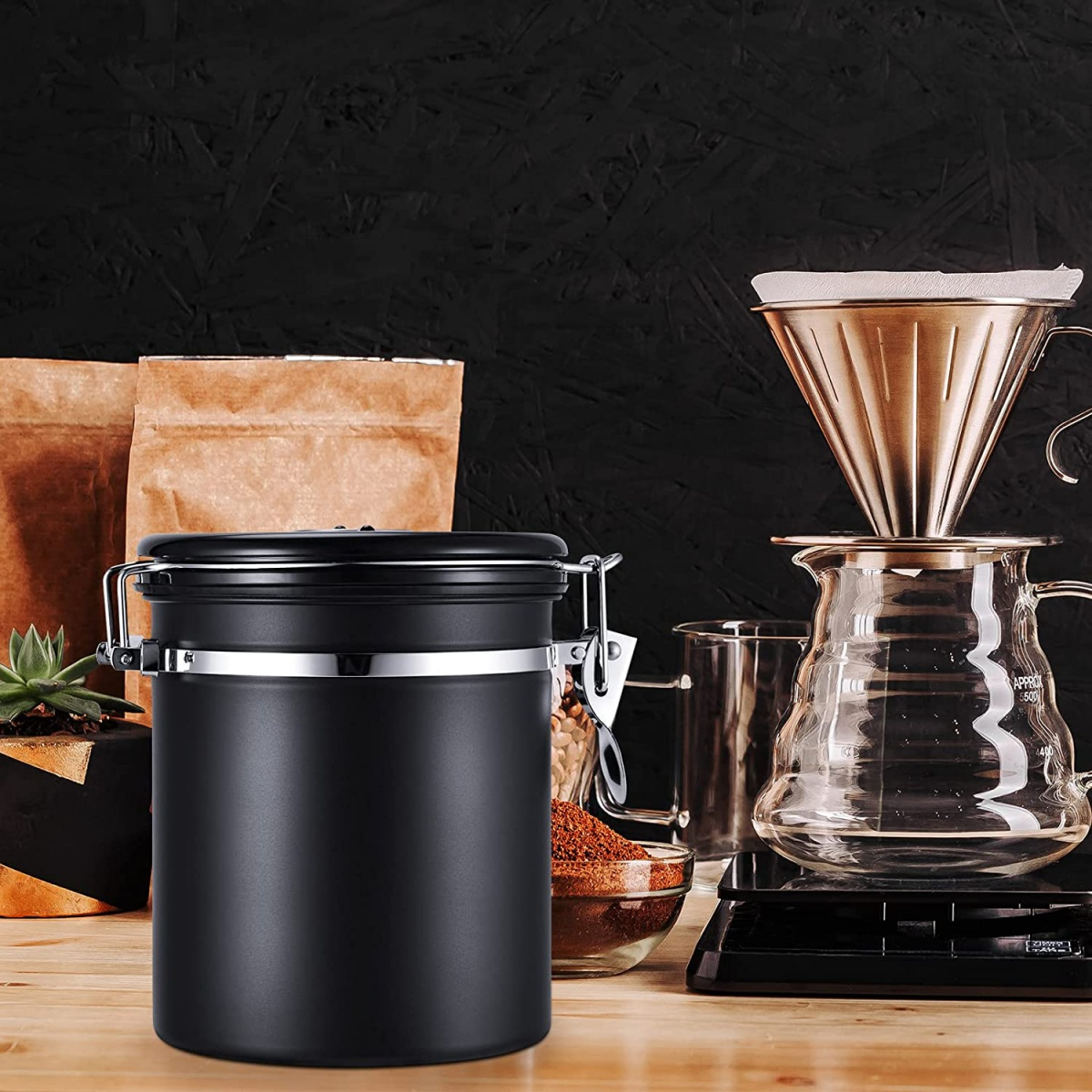 Ein schwarzer Kaffeebehälter steht neben Kaffeepulver, Papierbeuteln und einer Kaffeebrühvorrichtung.